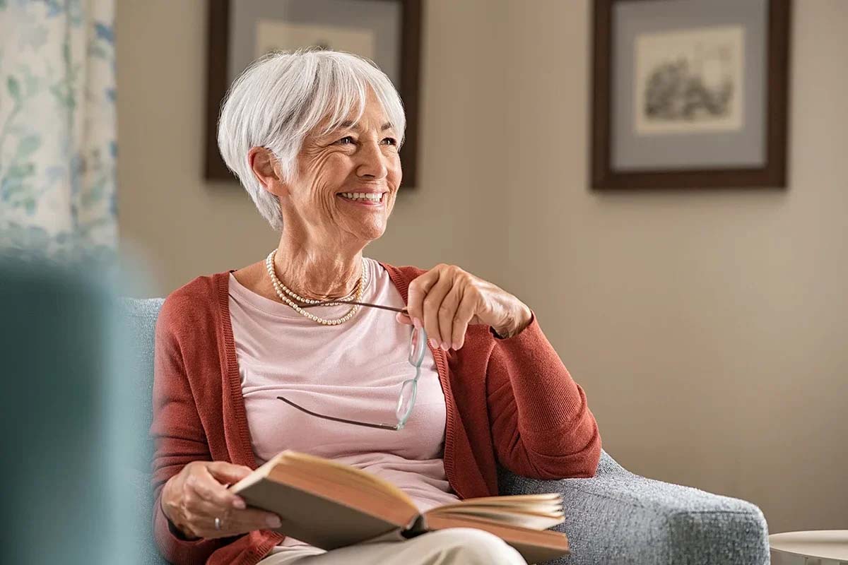 Smiling older woman reading a book in cozy setting.